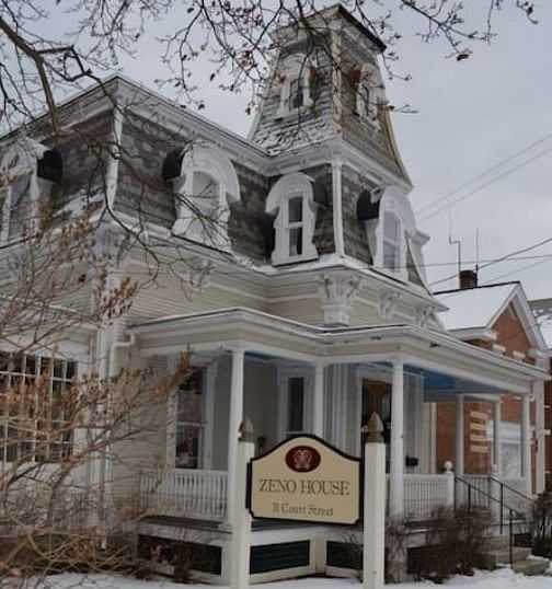Victorian-style house with a sign reading "Zeno House" in winter.