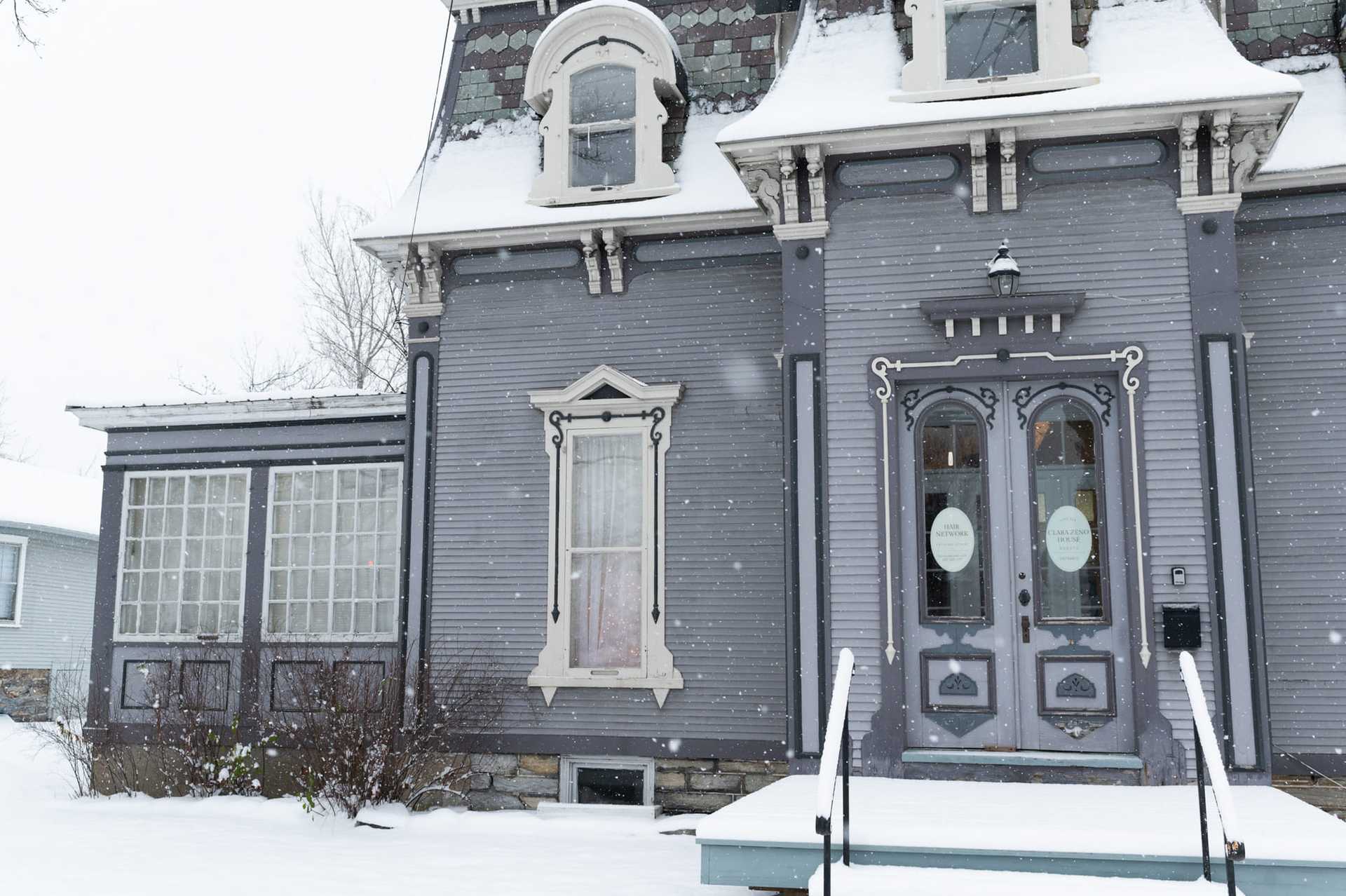 Victorian-style house in winter, with snow-covered roof and steps.