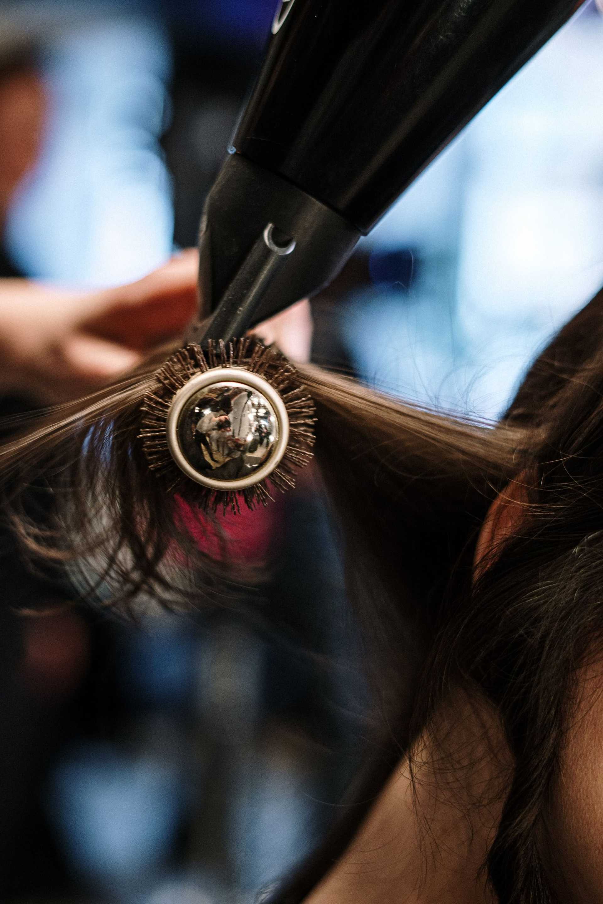 A hairstylist blow-drying hair with a round brush.