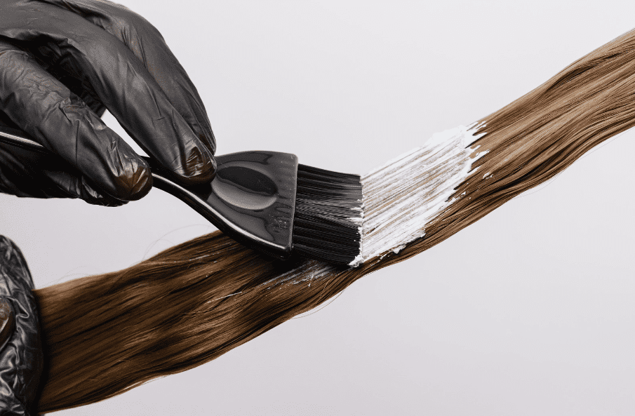 Applying hair dye to a strand of brown hair with a brush.